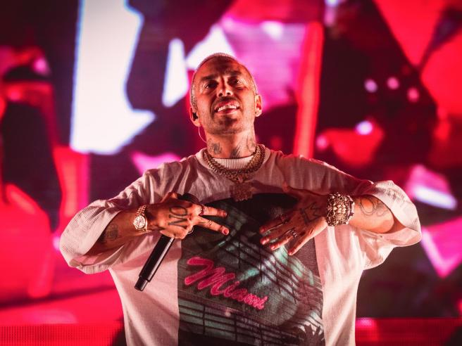 Il rapper Luchè durante un concerto dal vivo sul palco con luci rosse sullo sfondo.