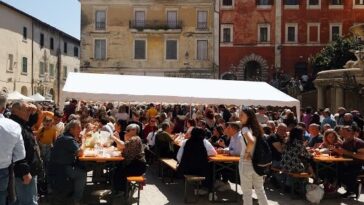 Persone sedute ai tavoli durante una sagra di paese nel Lazio con stand gastronomici e bancarelle.