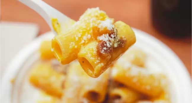 Primo piano di un piatto di carbonara con rigatoni, guanciale croccante e pecorino durante il festival a Roma Ostiense.