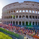 Migliaia di runner corrono davanti al Colosseo durante la Maratona di Roma tra transenne e pubblico.