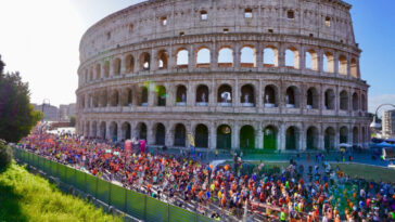 Migliaia di runner corrono davanti al Colosseo durante la Maratona di Roma tra transenne e pubblico.
