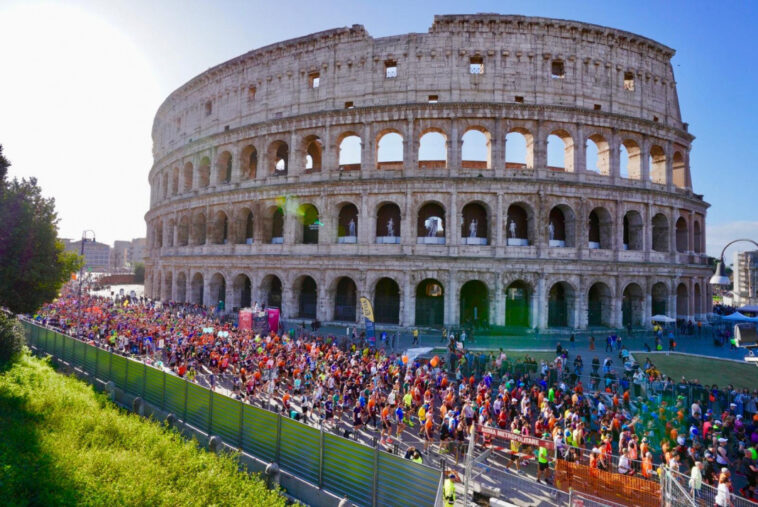 Migliaia di runner corrono davanti al Colosseo durante la Maratona di Roma tra transenne e pubblico.