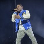 Ernia si esibisce sul palco durante un concerto con microfono in mano e luci sceniche sullo sfondo.