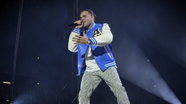 Ernia si esibisce sul palco durante un concerto con microfono in mano e luci sceniche sullo sfondo.