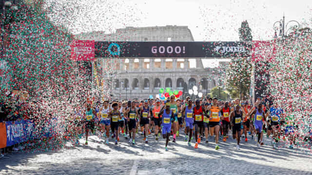 Runner alla partenza della Maratona di Roma davanti al Colosseo con coriandoli e arco di partenza.