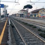 Binari e banchina della stazione di Pomezia con cartello visibile e linee ferroviarie.