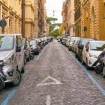 Auto parcheggiate lungo una strada del centro di Roma con strisce blu ai lati e file di veicoli su entrambi i lati.