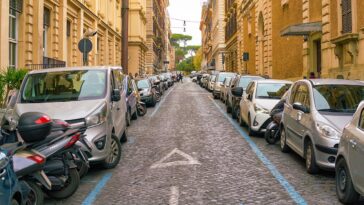 Auto parcheggiate lungo una strada del centro di Roma con strisce blu ai lati e file di veicoli su entrambi i lati.
