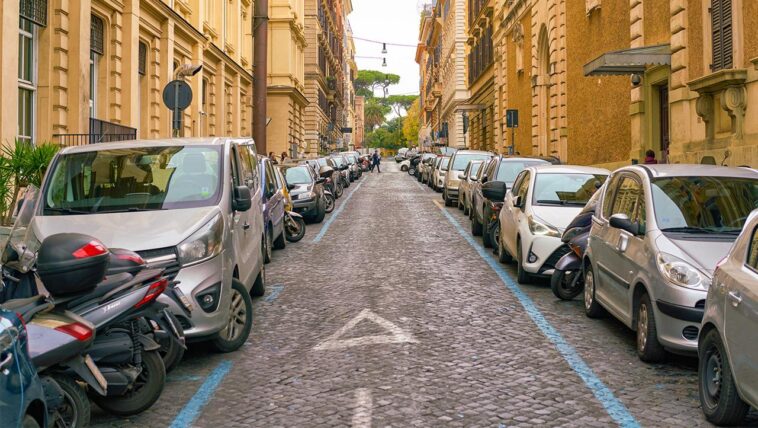 Auto parcheggiate lungo una strada del centro di Roma con strisce blu ai lati e file di veicoli su entrambi i lati.