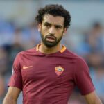 Mohamed Salah in campo con la maglia della Roma durante una partita, con espressione concentrata.