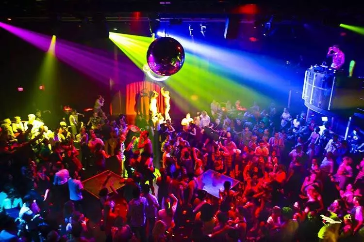 Discoteca affollata con luci colorate e pista da ballo piena di persone