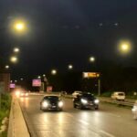 Traffico serale sulla Pontina illuminata dai lampioni, con auto in transito lungo la carreggiata.