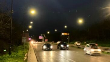 Traffico serale sulla Pontina illuminata dai lampioni, con auto in transito lungo la carreggiata.