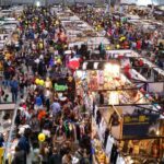 Folla di visitatori tra stand e padiglioni del Romics alla Fiera di Roma, con espositori dedicati a fumetti, videogiochi, gadget e cosplay.