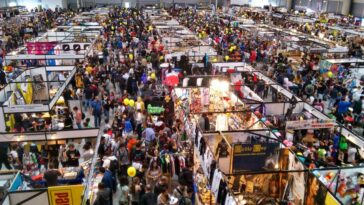 Folla di visitatori tra stand e padiglioni del Romics alla Fiera di Roma, con espositori dedicati a fumetti, videogiochi, gadget e cosplay.