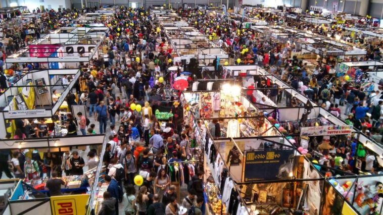 Folla di visitatori tra stand e padiglioni del Romics alla Fiera di Roma, con espositori dedicati a fumetti, videogiochi, gadget e cosplay.