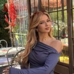 Ragazza giovane posa in un giardino con abito elegante e sfondo floreale.