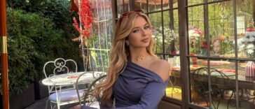 Ragazza giovane posa in un giardino con abito elegante e sfondo floreale.