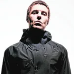 Liam Gallagher in posa con giacca scura su sfondo chiaro