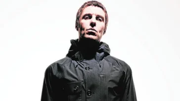 Liam Gallagher in posa con giacca scura su sfondo chiaro