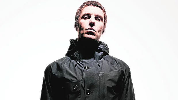 Liam Gallagher in posa con giacca scura su sfondo chiaro