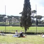 Persone rilassate su prato in un parco di Roma sotto il sole