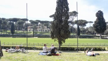 Persone rilassate su prato in un parco di Roma sotto il sole