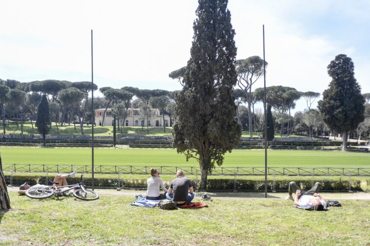 Persone rilassate su prato in un parco di Roma sotto il sole