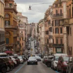 Strada di Roma con traffico e auto parcheggiate lungo i lati, palazzi storici ai bordi