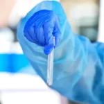 Operatore sanitario con guanto blu mentre tiene una provetta durante controlli di laboratorio