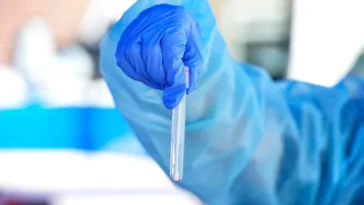 Operatore sanitario con guanto blu mentre tiene una provetta durante controlli di laboratorio