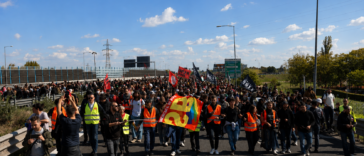 Corteo di manifestanti e lavoratori durante uno sciopero con bandiere e giubbotti catarifrangenti