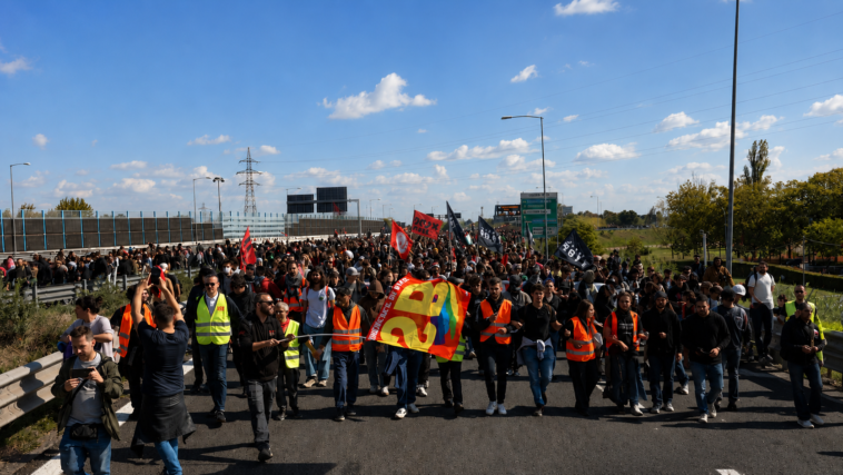 Corteo di manifestanti e lavoratori durante uno sciopero con bandiere e giubbotti catarifrangenti