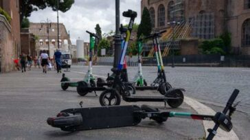 Monopattini elettrici parcheggiati e uno caduto a terra in una strada del centro di Roma vicino ai Fori Imperiali.