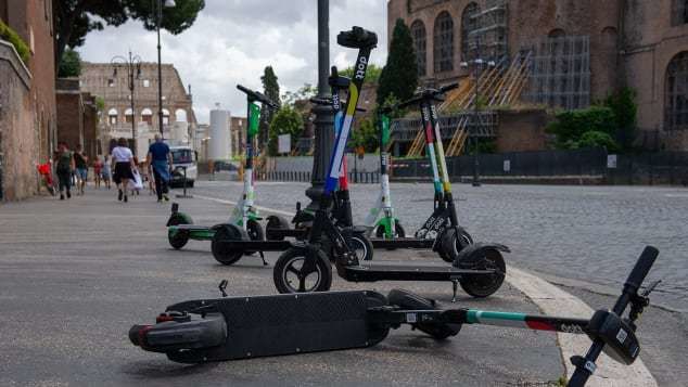 Monopattini elettrici parcheggiati e uno caduto a terra in una strada del centro di Roma vicino ai Fori Imperiali.
