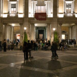 Persone in fila davanti ai Musei Capitolini illuminati durante la Notte dei Musei a Roma, con visitatori che affollano Piazza del Campidoglio nelle ore serali.