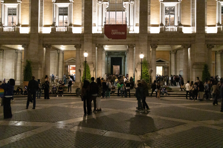 Persone in fila davanti ai Musei Capitolini illuminati durante la Notte dei Musei a Roma, con visitatori che affollano Piazza del Campidoglio nelle ore serali.