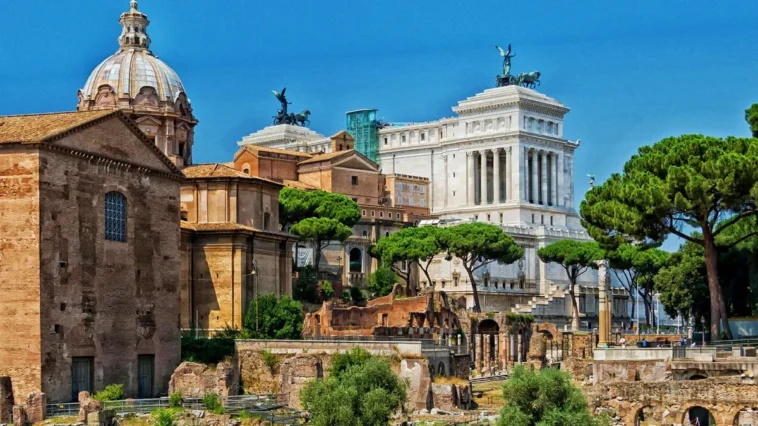 Vista panoramica dei Fori Imperiali di Roma con il Vittoriano sullo sfondo, tra rovine archeologiche, pini romani e monumenti storici nel cuore della Capitale.