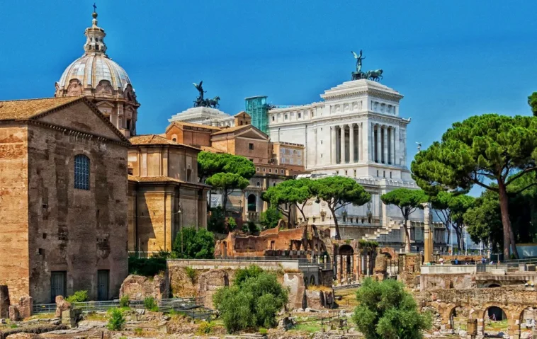 Vista panoramica dei Fori Imperiali di Roma con il Vittoriano sullo sfondo, tra rovine archeologiche, pini romani e monumenti storici nel cuore della Capitale.