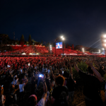 Migliaia di persone assistono a un grande concerto all'aperto a Roma durante la notte, con palco illuminato, schermi giganti e pubblico che alza le mani verso la scena.