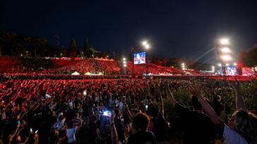 Migliaia di persone assistono a un grande concerto all'aperto a Roma durante la notte, con palco illuminato, schermi giganti e pubblico che alza le mani verso la scena.