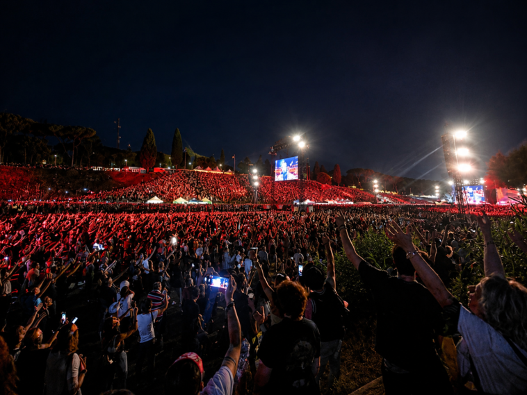 Migliaia di persone assistono a un grande concerto all'aperto a Roma durante la notte, con palco illuminato, schermi giganti e pubblico che alza le mani verso la scena.