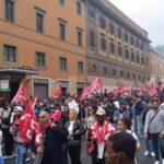 Manifestazione con centinaia di persone in corteo lungo una strada del centro di Roma, tra bandiere sindacali e striscioni, durante una protesta che ha richiamato partecipanti da diverse città italiane.