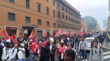 Manifestazione con centinaia di persone in corteo lungo una strada del centro di Roma, tra bandiere sindacali e striscioni, durante una protesta che ha richiamato partecipanti da diverse città italiane.
