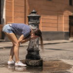 Ragazza si rinfresca a una fontanella nel centro di Roma durante una giornata di forte caldo estivo.