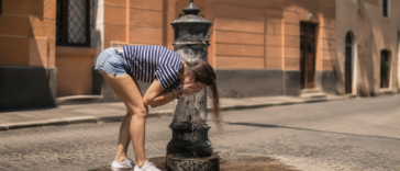 Ragazza si rinfresca a una fontanella nel centro di Roma durante una giornata di forte caldo estivo.