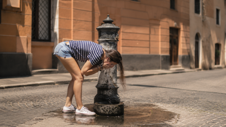 Ragazza si rinfresca a una fontanella nel centro di Roma durante una giornata di forte caldo estivo.