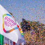 Bandiera del Roma Pride sventola tra coriandoli colorati durante la parata, con i colori dell’arcobaleno protagonisti della manifestazione nel centro della Capitale.