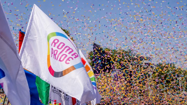 Bandiera del Roma Pride sventola tra coriandoli colorati durante la parata, con i colori dell’arcobaleno protagonisti della manifestazione nel centro della Capitale.