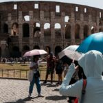 Turisti si proteggono dal sole con ombrelli davanti al Colosseo durante una giornata di forte caldo a Roma, mentre le temperature superano i 35 gradi.